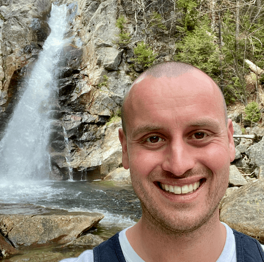Alex Julian smiling in front of a waterfall